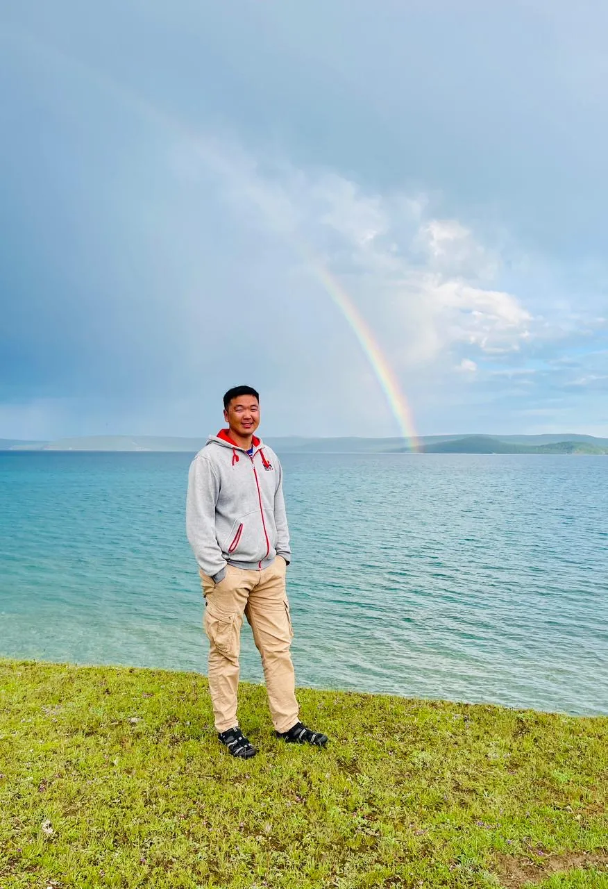 Buya, the tour leader, standing on the shore of an alpine lake under a rainbow.