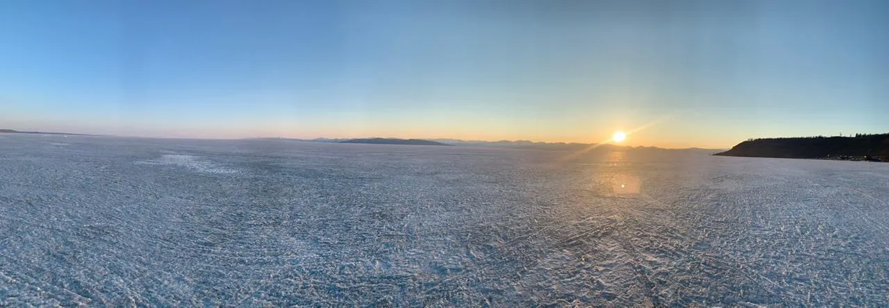 Sunset across a frozen lake, distant Mongolian mountains receding into a peach-blue horizon.