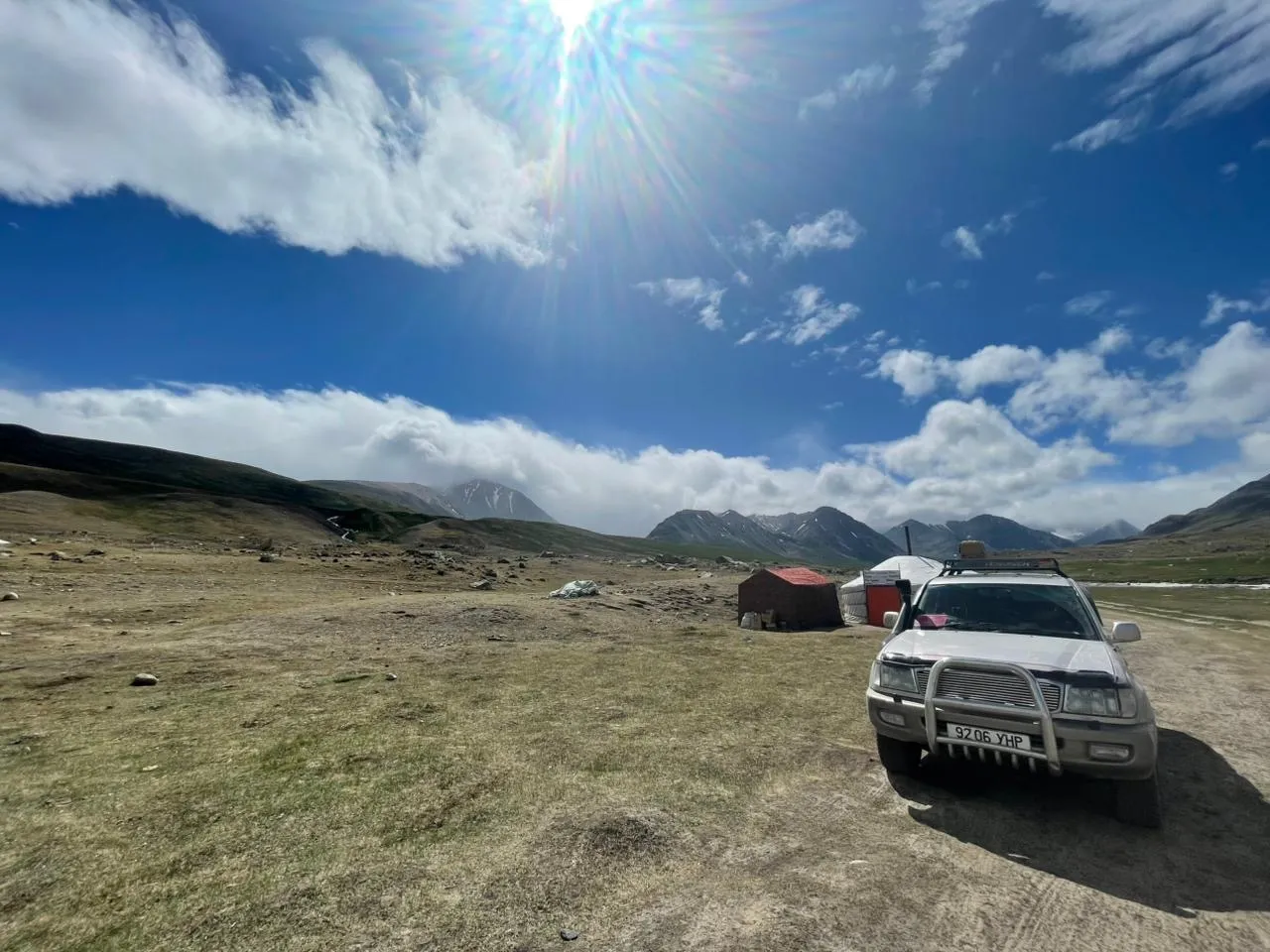 A Land Cruiser parked beside a small ger camp at the edge of the Altai mountains, mid-afternoon.